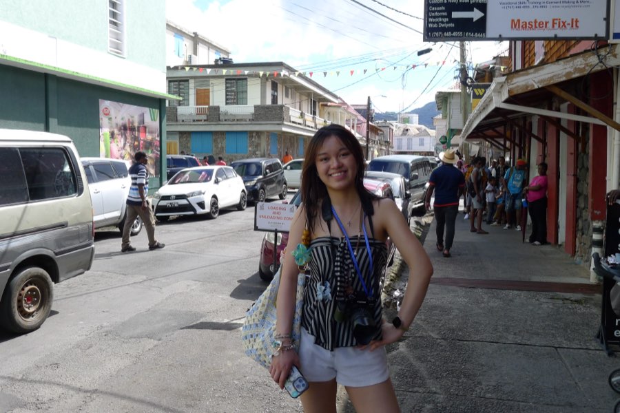 Smiling with a camera and tote bag on a sunny street in Dominica